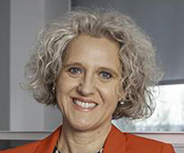 A woman with blonde short curly hair and a red blazer on