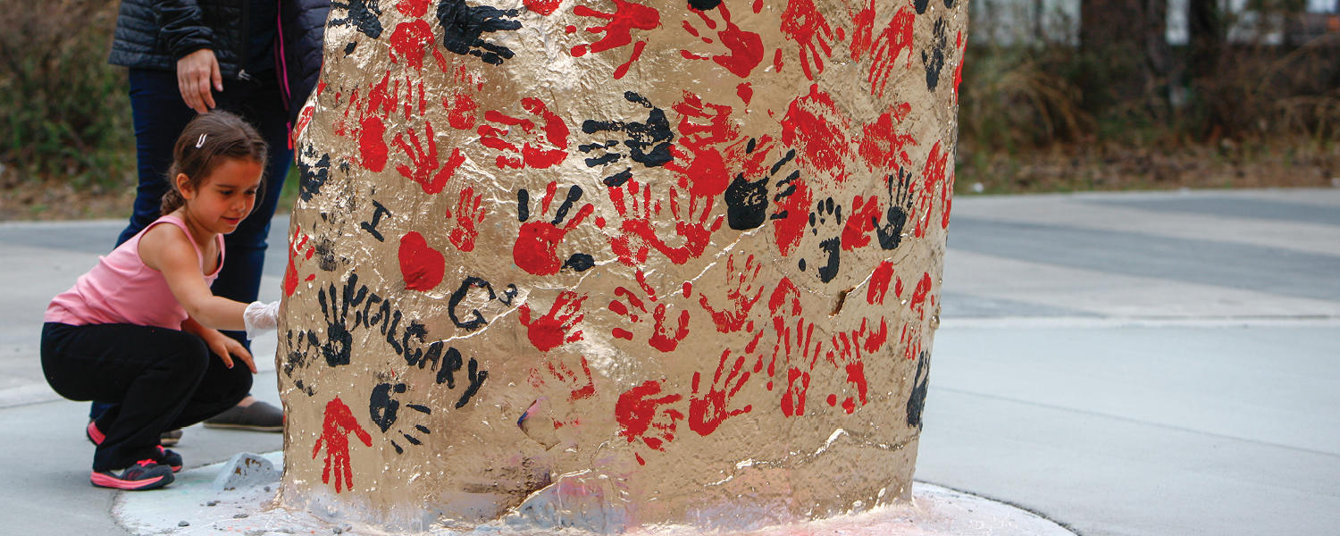 Young girl adds her hand print to a rock painted red and gold
