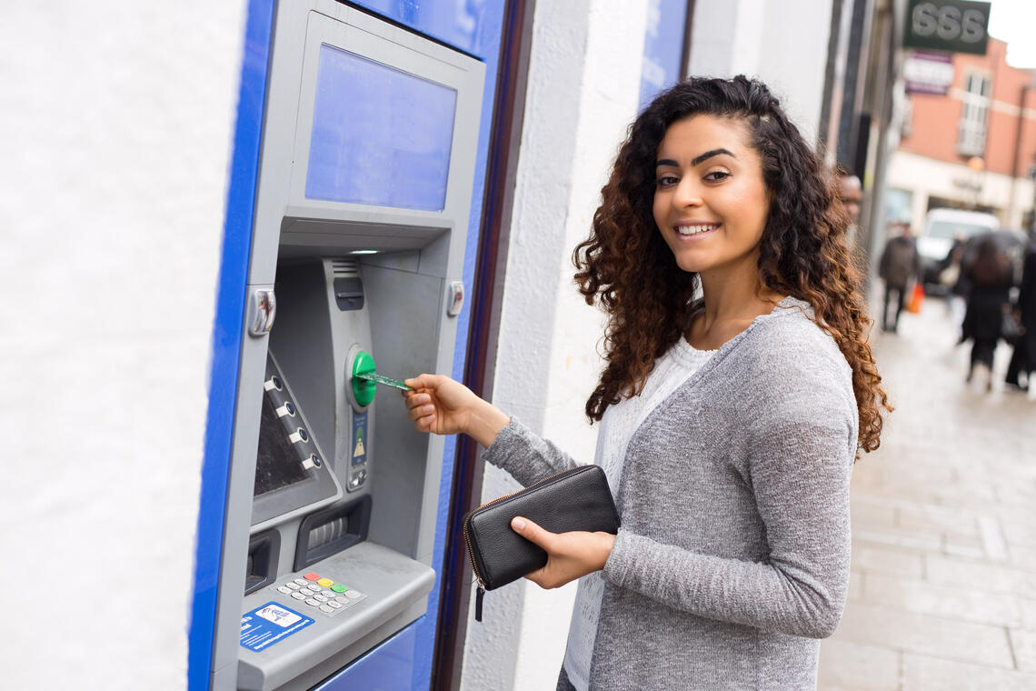 woman standing at a bank machine, smiling at the camera 