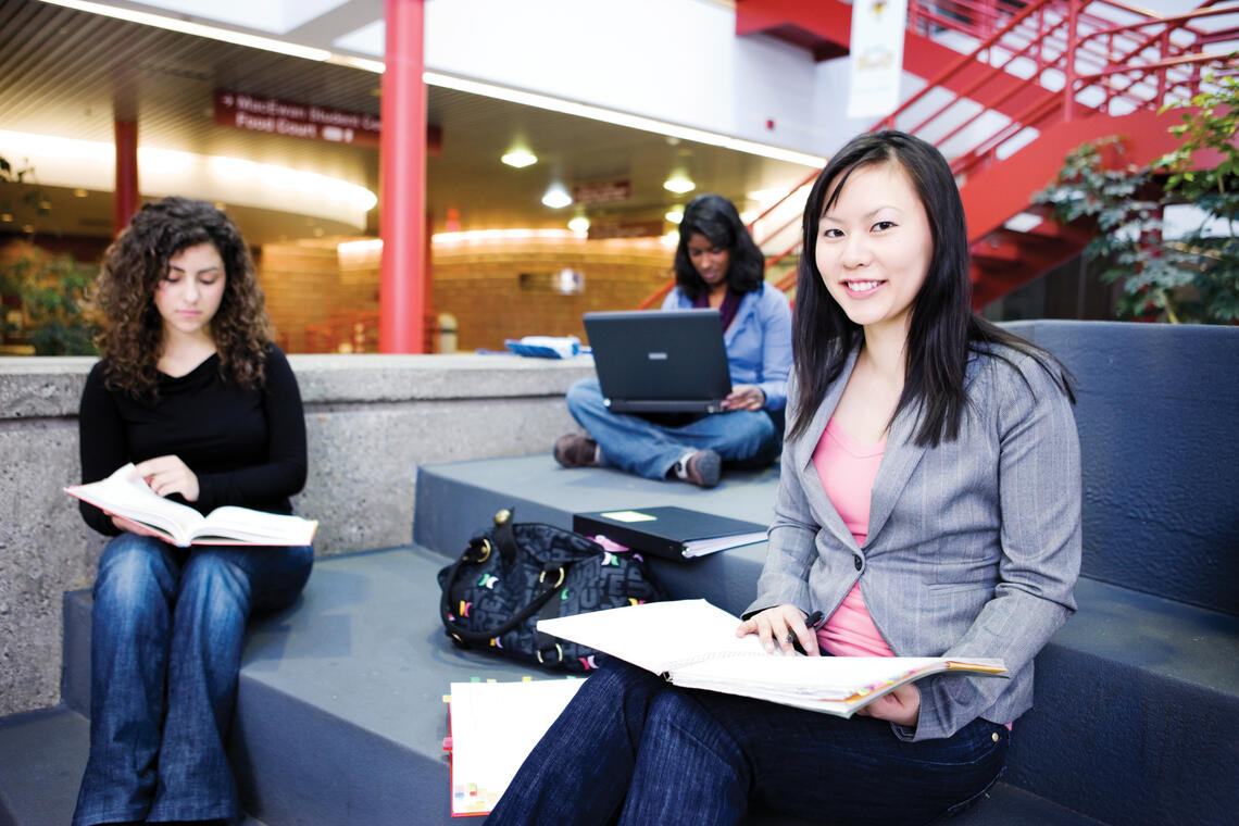 Three women sitting on stair in kinesiology atrium holding notebooks.