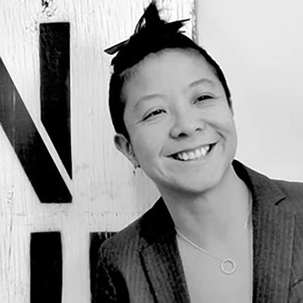 Woman with short dark hair smiles in front of grafitti