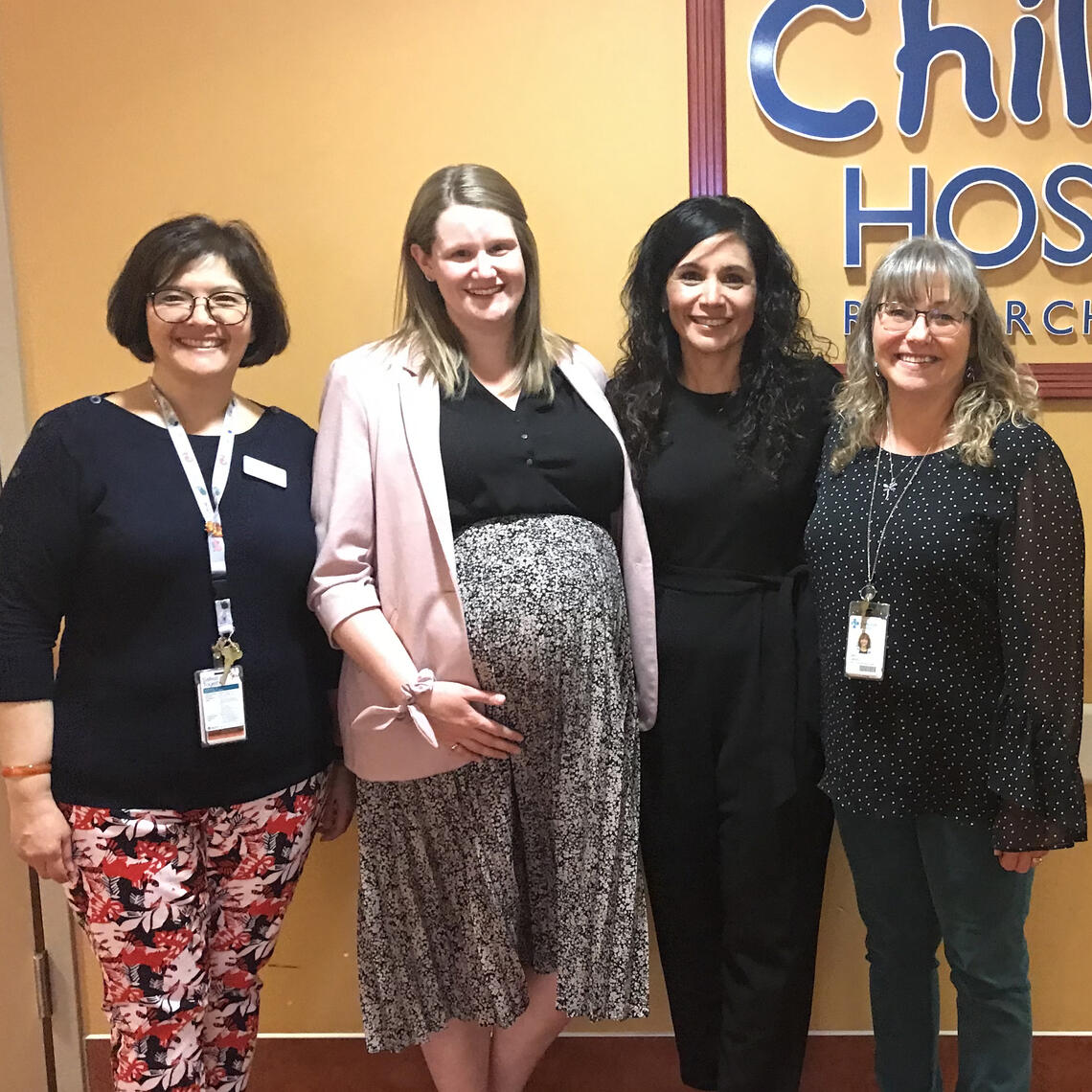 A group of women in stand in front of the Alberta Children's Hospital Sign