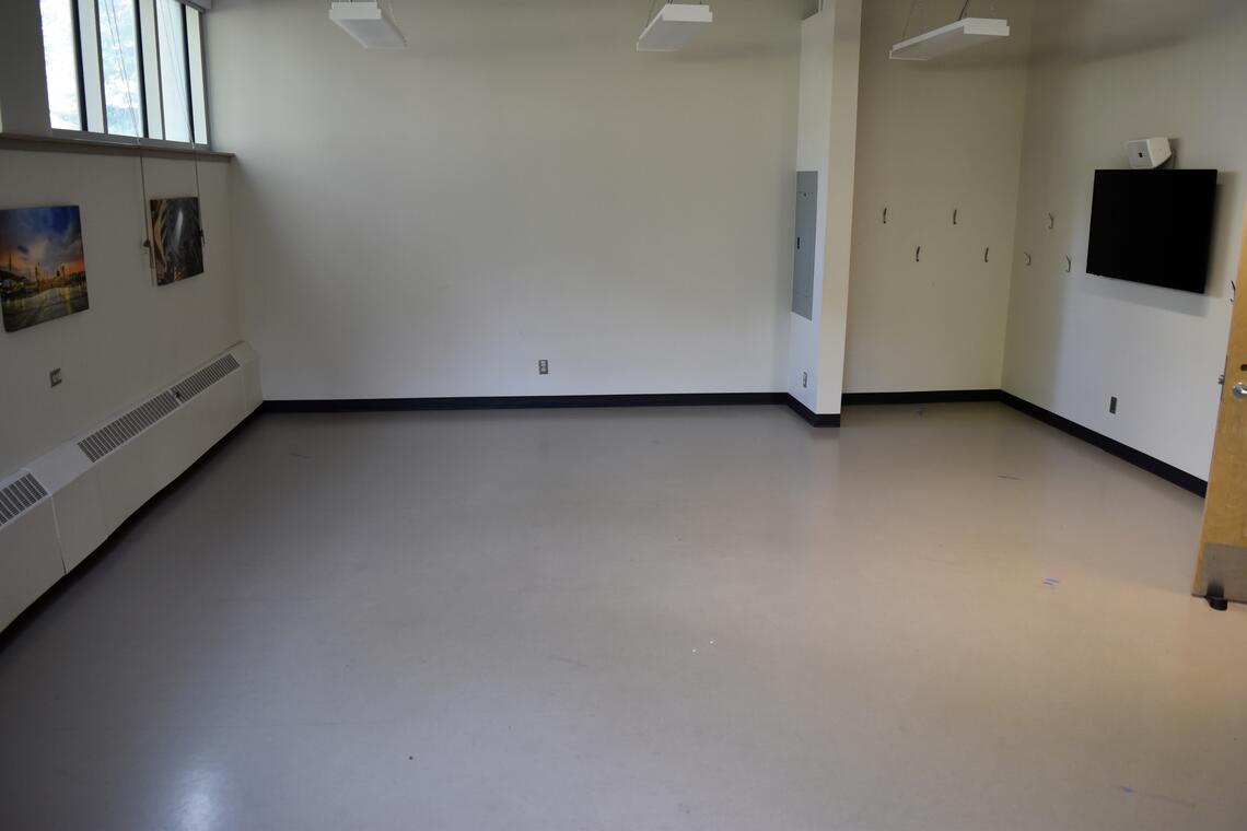 empty white room with paintings, a tv screen, and coat hooks on the wal