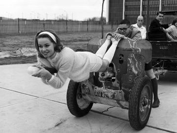 Student riding the barrel of a Second World War field gun that is being towed by a Willys Jeep during Bermuda Shorts Day.