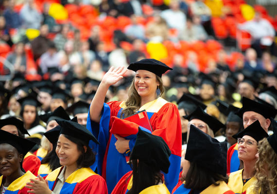 An image of a student standing up amongst graduates and waving 