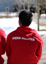 Two students in peer helper hoodies sitting outside