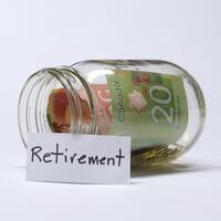A mason jar with money billsd and a sign that says "retirement" placed in front