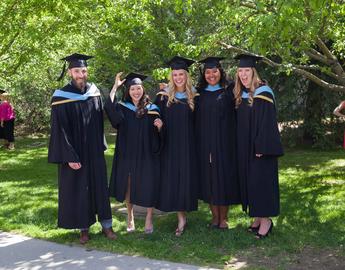 Five graduates standing in a line, smiling 