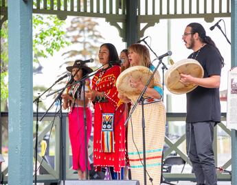 A group of Indigenous performers play drums and sing in a gazebo