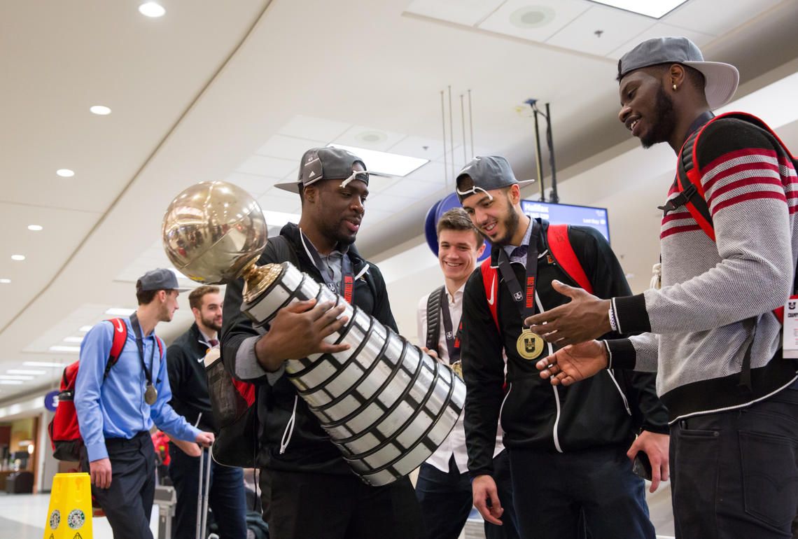 Jhony Verrone cradles the trophy, as author of the game-winning basket Mambi Diawara, far right, reaches for his turn. Teammate Sasha Pojuzina looks on.