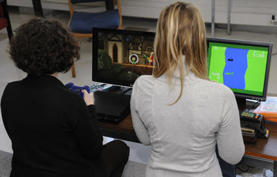 The library is installing six PC stations for researchers to play games on newer consoles. Student Heather Gagnon plays alongside librarian Dr. Alix Hayden.