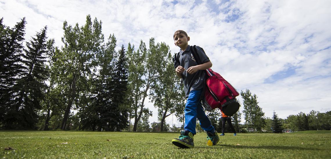 Summer camper walks across campus carrying a red golf bag