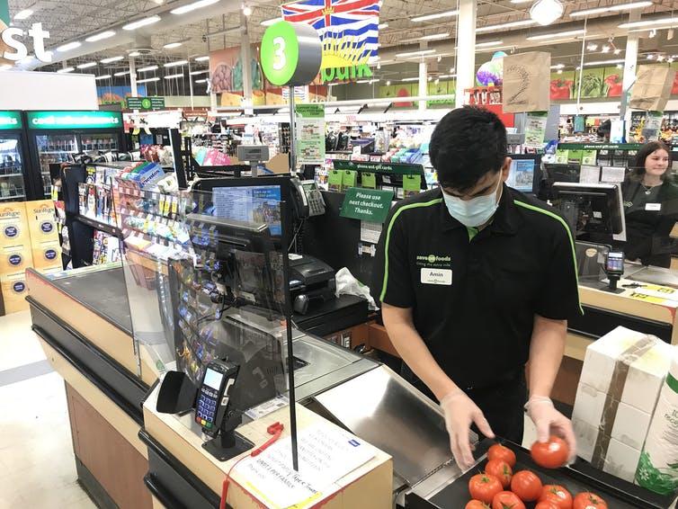A Plexiglas barrier protects a cashier at a grocery store in North Vancouver, B.C., in March 2020