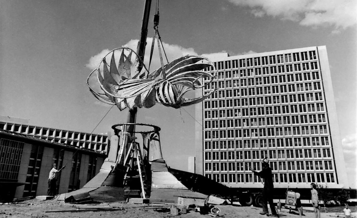 Image of a crane lowering the top of the Norris Sculpture (also known as The Prairie Chicken) onto the base