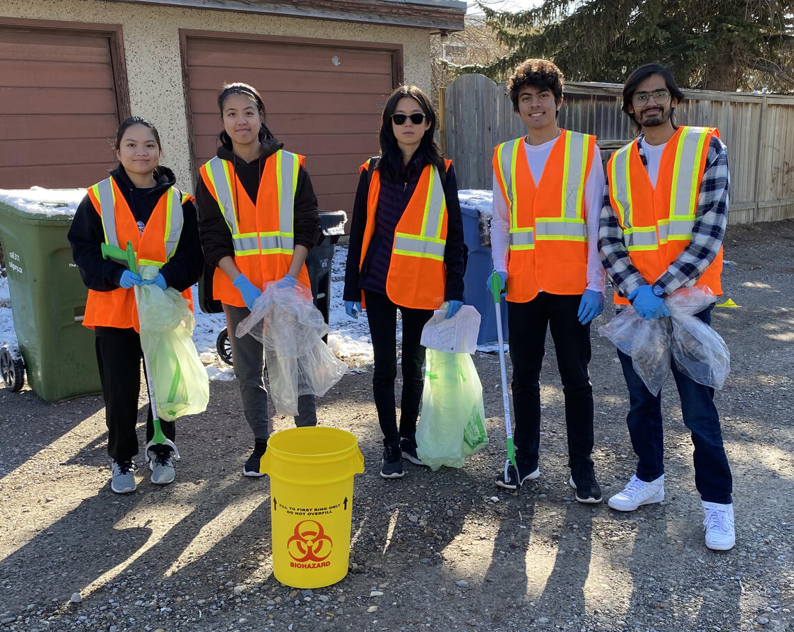 Group of student volunteers standing together in a neighbouring community, wearing high-visibility vests and holding garbage bags. 