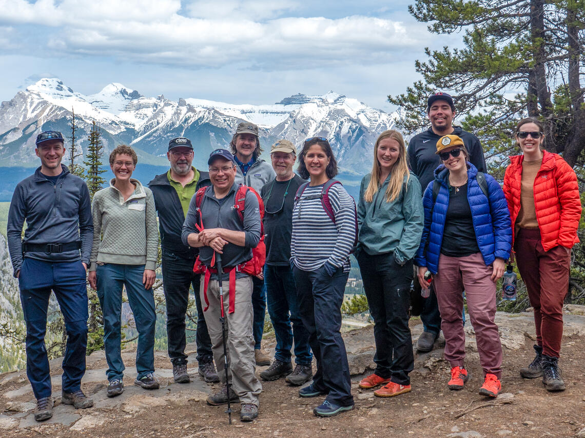 A group of people wearing hiking gear standing on a hiking trail with a mountain in the background