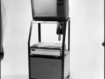 An audio visual stand that holds a television and a Sony video cassette machine. A rotary-dial phone is also attached to the stand. 1972. UARC84.005_14.39