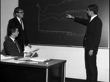 Three commerce students in the Faculty of Business work at a blackboard as part of a computer game. 1967. UARC82.011.3.12