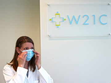 A health care provider tries on a mask in front of a sign that reads W21C