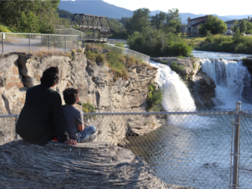 Silhouette of an adult and child sitting on a large rock overlooking a waterfall.