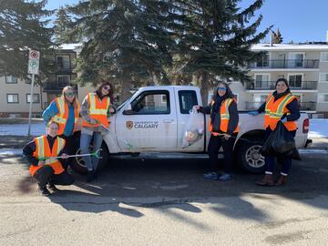 Volunteers wearing high-vis vests and holding trash bags, posing in front of a UCalgary vehicle.