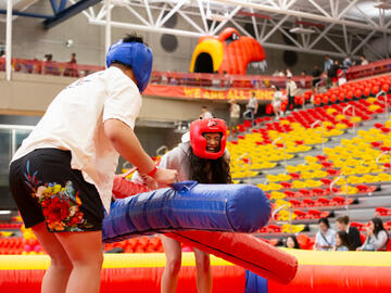Two people dressed in helmets play on a bouncy castle