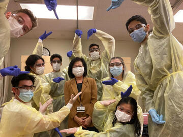 Nursing students in full PPE with masks and instructor standing in the middle. 