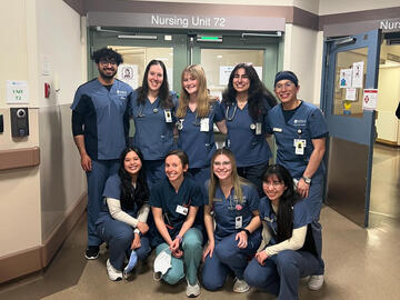 Nursing students in scrubs standing in front of unit entrance at hospital.