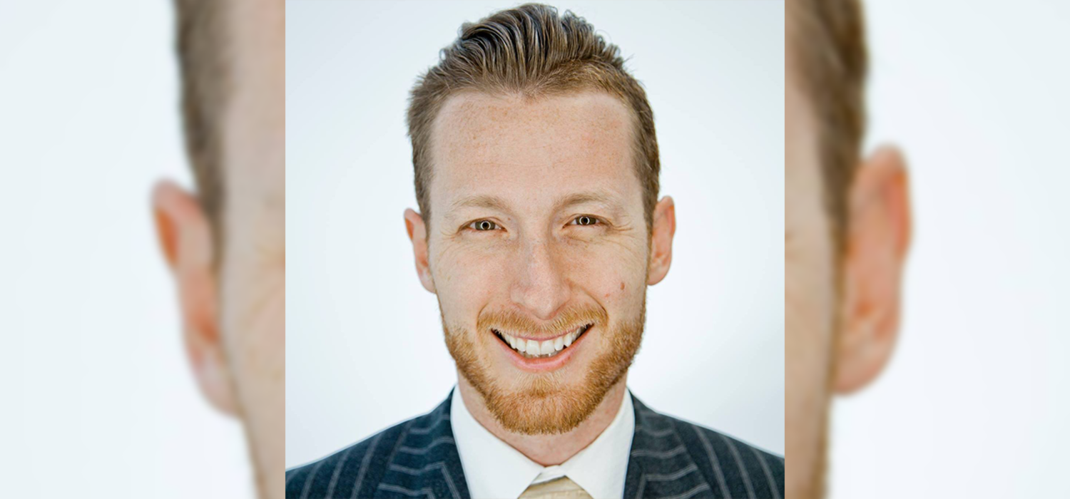 Alumnus Michael J. Burak smiles in close up. He is wearing a suit and standing against a white background