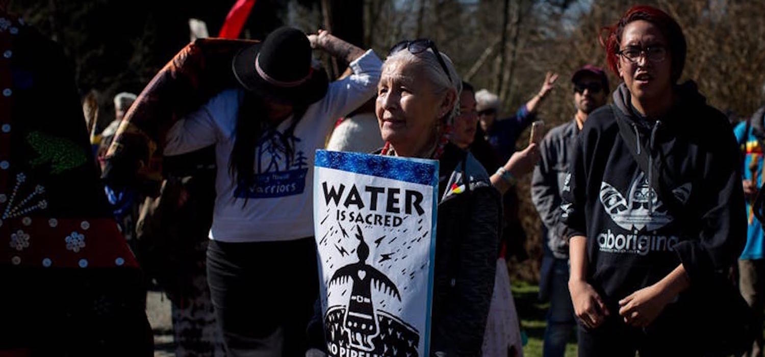 An Indigenous woman holds a sign as thousands of people attend a protest against the Kinder Morgan Trans Mountain pipeline expansion in Burnaby, B.C., on March 10, 2018. 
