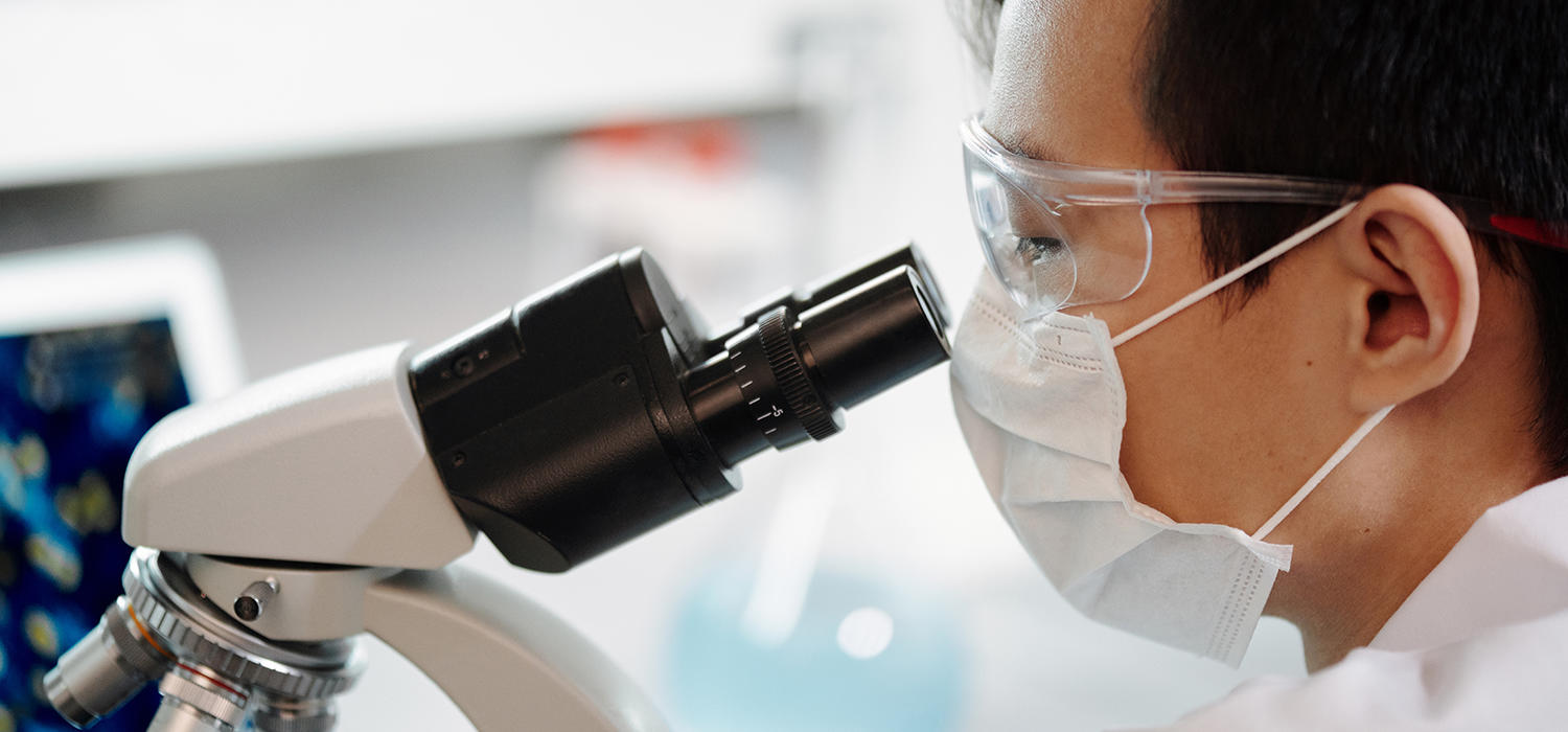 Man with glasses and mask looking through microscope