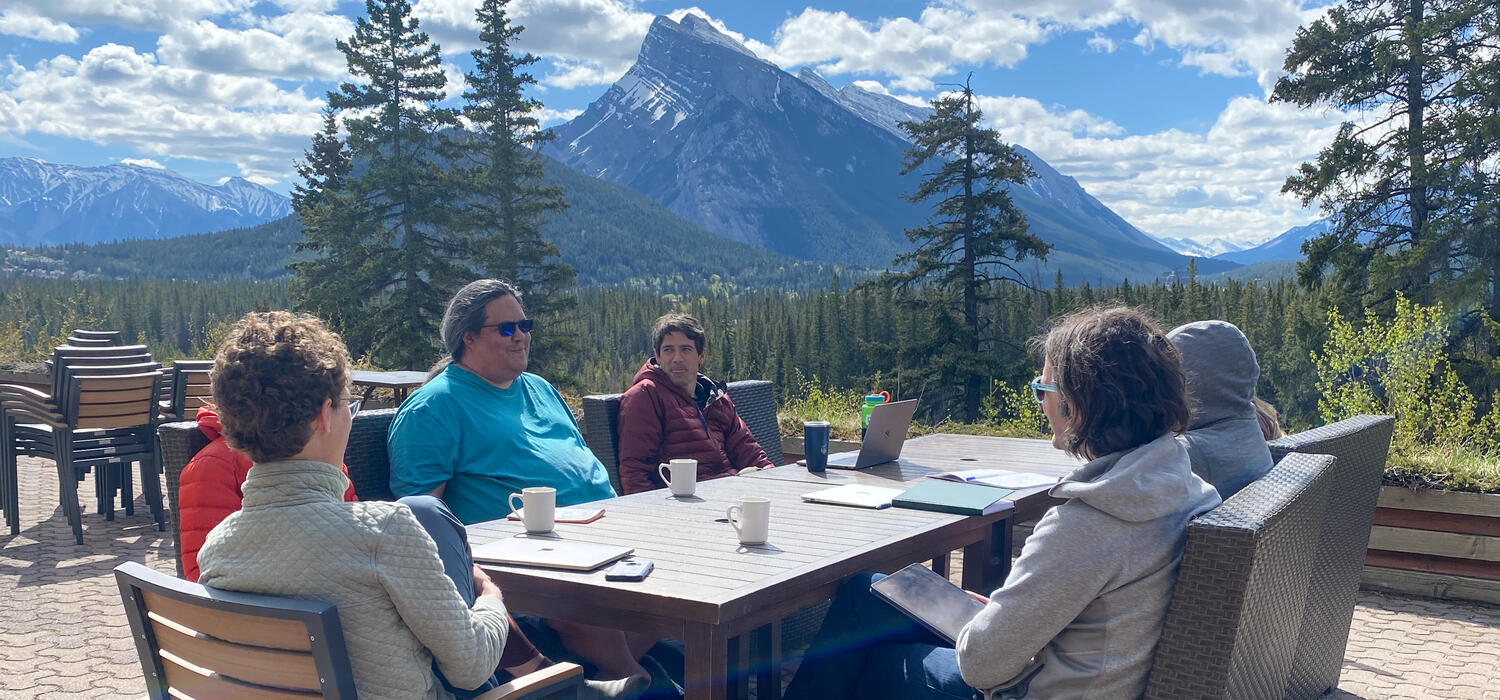 People sitting around a table with a mountain in the background 