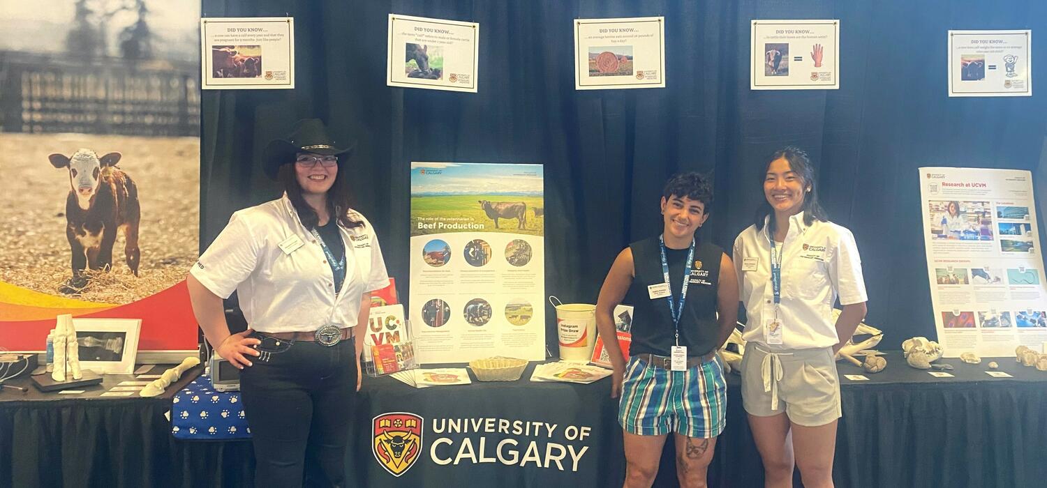 Three people stand in front of a University of Calgary Vet Med booth at the Calgary Stampede
