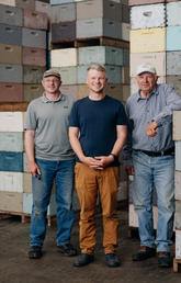 Three men stand in front of palettes of honey