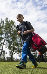 Summer camper walks across campus carrying a red golf bag