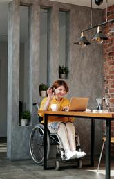 A woman in a wheelchair waving at computer screen