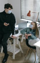 Two teenagers wearing face masks, one holding a cell phone