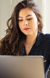 A woman sits at a laptop. There is a small gold statue of Lady Justice on the table next to her.