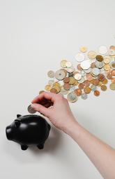 A hand places coins into a black piggy bank.