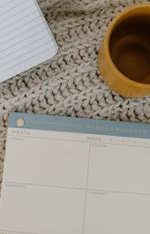 An overhead view of a weekly planner with a pencil next to it.