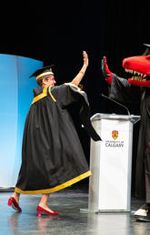 Chancellor Emerita Deborah Yedlin and Rex on the UCalgary convocation stage, giving each other a high five while wearing graduation gowns.