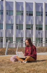 A student sits in the grass while using a computer.