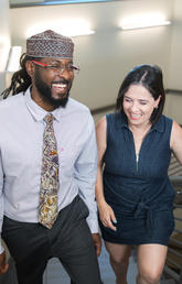 Two students walk up a flight of stairs. They are smiling and laughing.