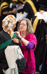 Two volunteers help graduates get ready to walk the stage.