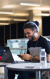 Student in TFDL using mobile device and laptop.