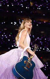 Taylor Swift during Eras Tour in purple dress holding blue guitar