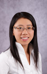 A headshot of a woman with long black hair and glasses