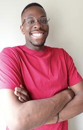 A man wearing glasses and a red shirt smiles at the camera