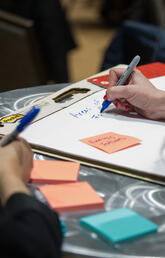 People write on colourful sticky notes on a silver table