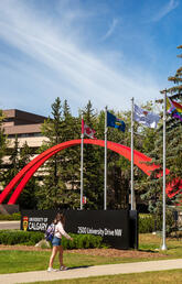 People walk past the iconic red arch that marks the main entrance to the UCalgary campus